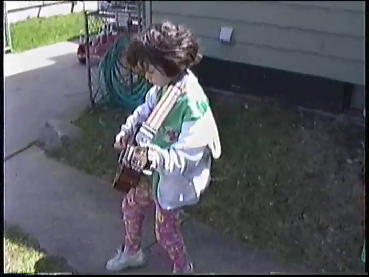 a young Lee playing a JCPenney acoustic guitar in the backyard